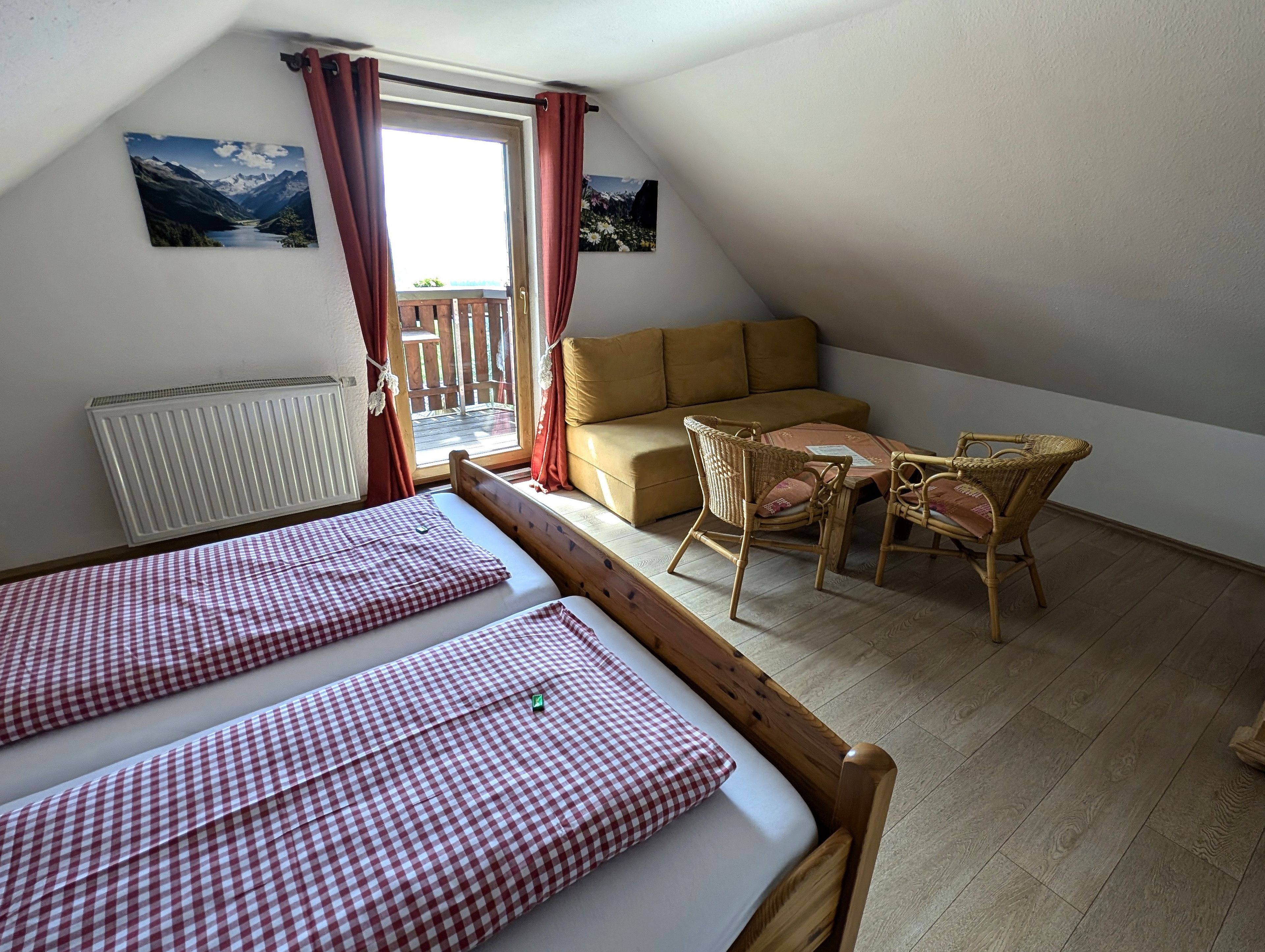 A cozy room with a bed, a sofa, a table with chairs, a radiator, and a window with curtains.