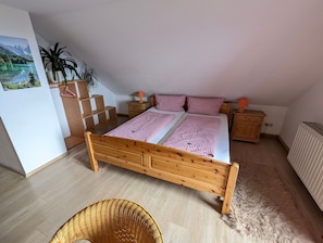 Une chambre à coucher avec un lit en bois, deux tables de chevet, une étagère fixée au mur et une plante suspendue.