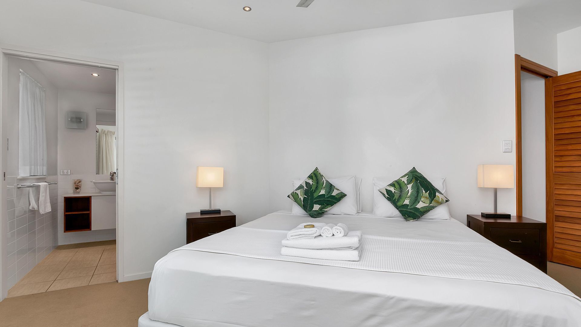 A hotel room with a large bed, two bedside tables with lamps, a wooden door, and a bathroom visible through an open door.