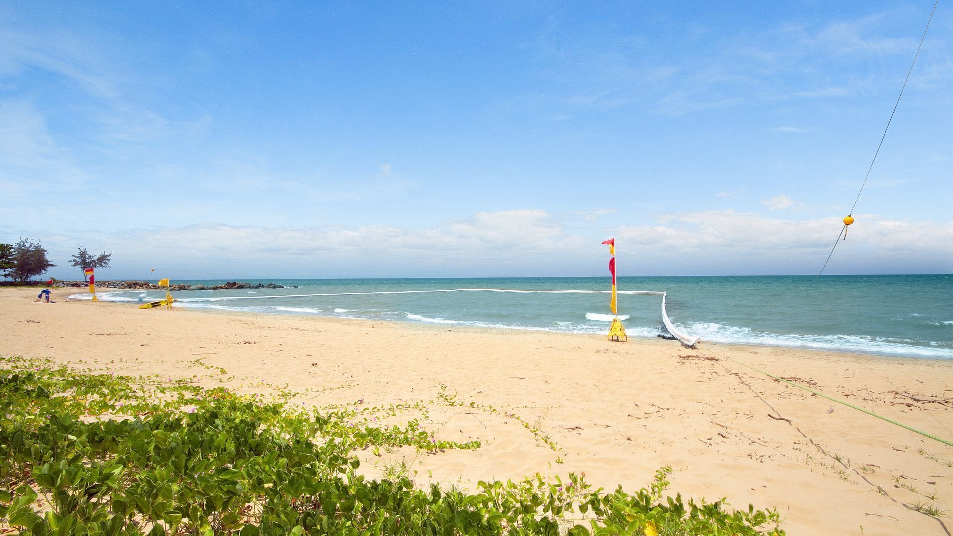 A beach with a lifeguard tower, a yellow buoy, and a rope extending into the water.