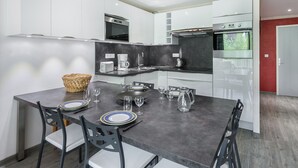 Une cuisine moderne avec des meubles blancs, un plan de travail noir et un coin repas avec une table dressée pour quatre personnes.