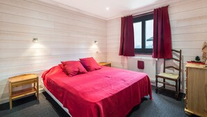 Une chambre à coucher avec un lit, une chaise en bois, une petite table et une fenêtre avec des rideaux.