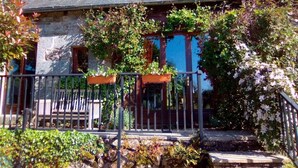 Ein Haus aus Stein mit dunklem Dach, einer Holzveranda und einem Metallgeländer.