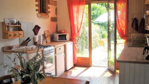 Eine Küche mit Holztisch, Herd, Mikrowelle und Spüle. Ein Fenster mit Vorhängen bietet Blick ins Freie.