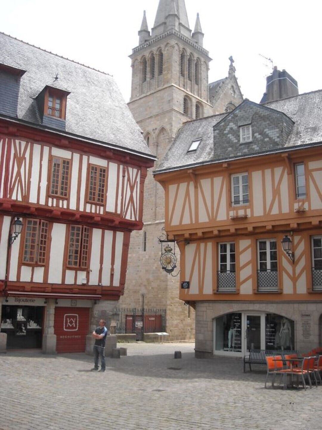A historic building with a traditional half-timbered facade, a prominent tower in the background, and a cobblestone street.