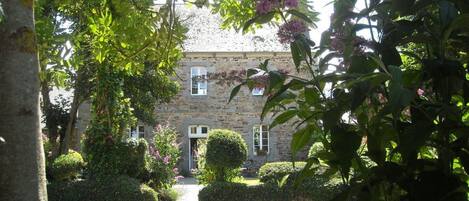 A stone building with a symmetrical facade, surrounded by well-maintained hedges and flowering plants.