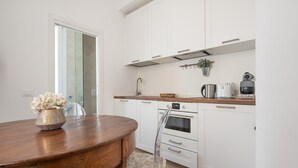 A modern kitchen with white cabinets, a wooden countertop, and a stainless steel kettle.