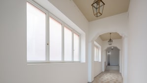 A long, narrow hallway with large windows on one side and a staircase leading to another level.