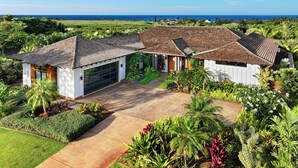A modern house with a large driveway, surrounded by lush greenery and a view of the ocean.