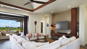 A modern living room with a large sectional sofa, a flat-screen TV mounted on the wall, and a view of the outdoors.