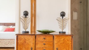 A wooden cabinet with two decorative spheres on top, a green leaf-shaped bowl, and a bed with floral bedding in the background. - Venetian Palace Red Apartment R&R (Venecia)