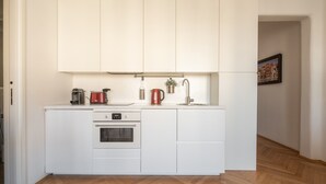 A compact kitchen with white cabinets, a built-in oven, a coffee maker, and a kettle. - Venetian Palace Red Apartment R&R (Venecia)