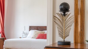 A neatly made bed with white linens and a red pillow, a wooden nightstand with a lamp, and a wooden dresser with a decorative lamp. - Venetian Palace Red Apartment R&R (Venecia)
