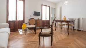 Un vaste salon doté d’un parquet en bois, d’une table à manger avec des chaises, d’un canapé et d’un téléviseur fixé au mur.