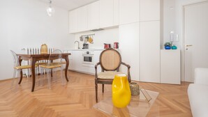 Une cuisine moderne avec des meubles blancs, une table à manger avec des chaises et un vase jaune posé sur une table en verre.