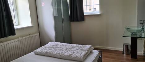 A bedroom with a bed, a wardrobe, a window with curtains, and a bathroom with a glass sink.