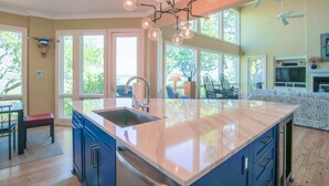 A spacious kitchen with a large island, a dining area with a bench, and a view of the outdoors through large windows.