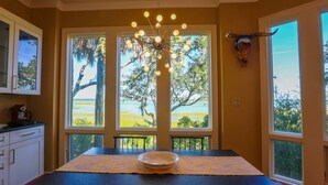 A dining area with a table set for two, large windows with a view of trees and water, and a unique light fixture above the table.