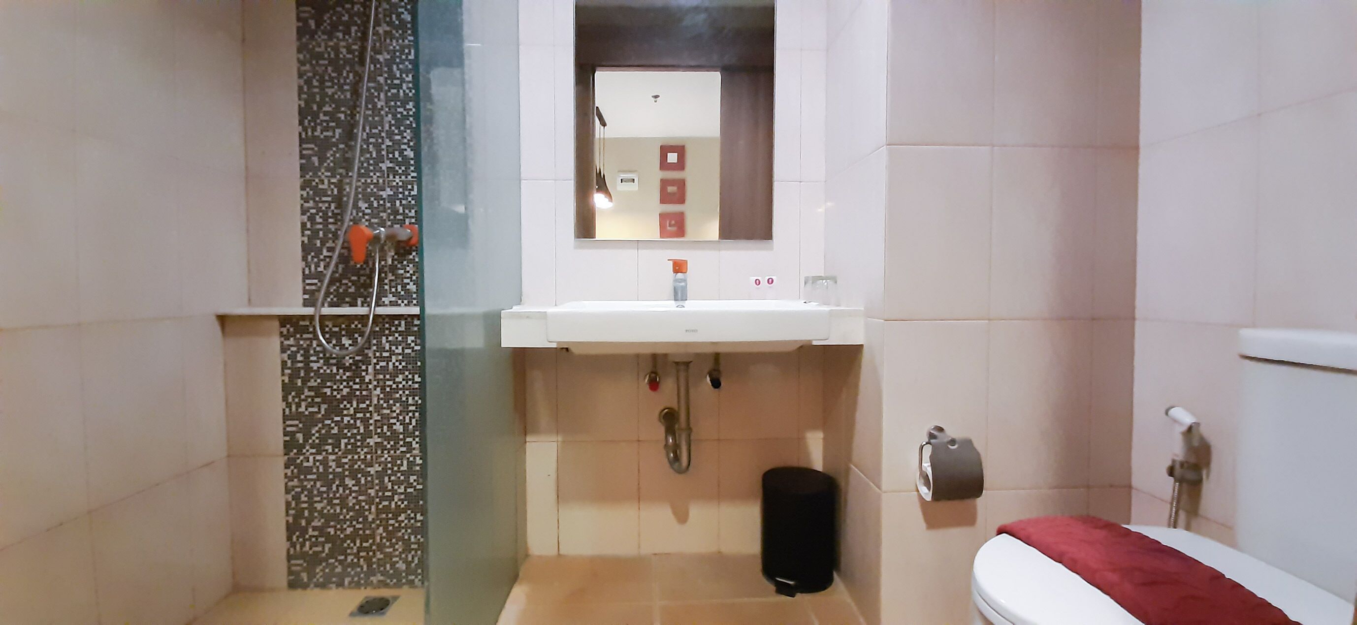 Une salle de bain avec une douche à parois de verre, un lavabo blanc avec un miroir au-dessus, et des toilettes avec une serviette rouge.