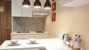 Une cuisine moderne avec un plan de travail blanc, un évier et un pare-feu en carreaux. On y trouve deux bols sur le plan de travail, une bouilloire et deux bouteilles d’eau.