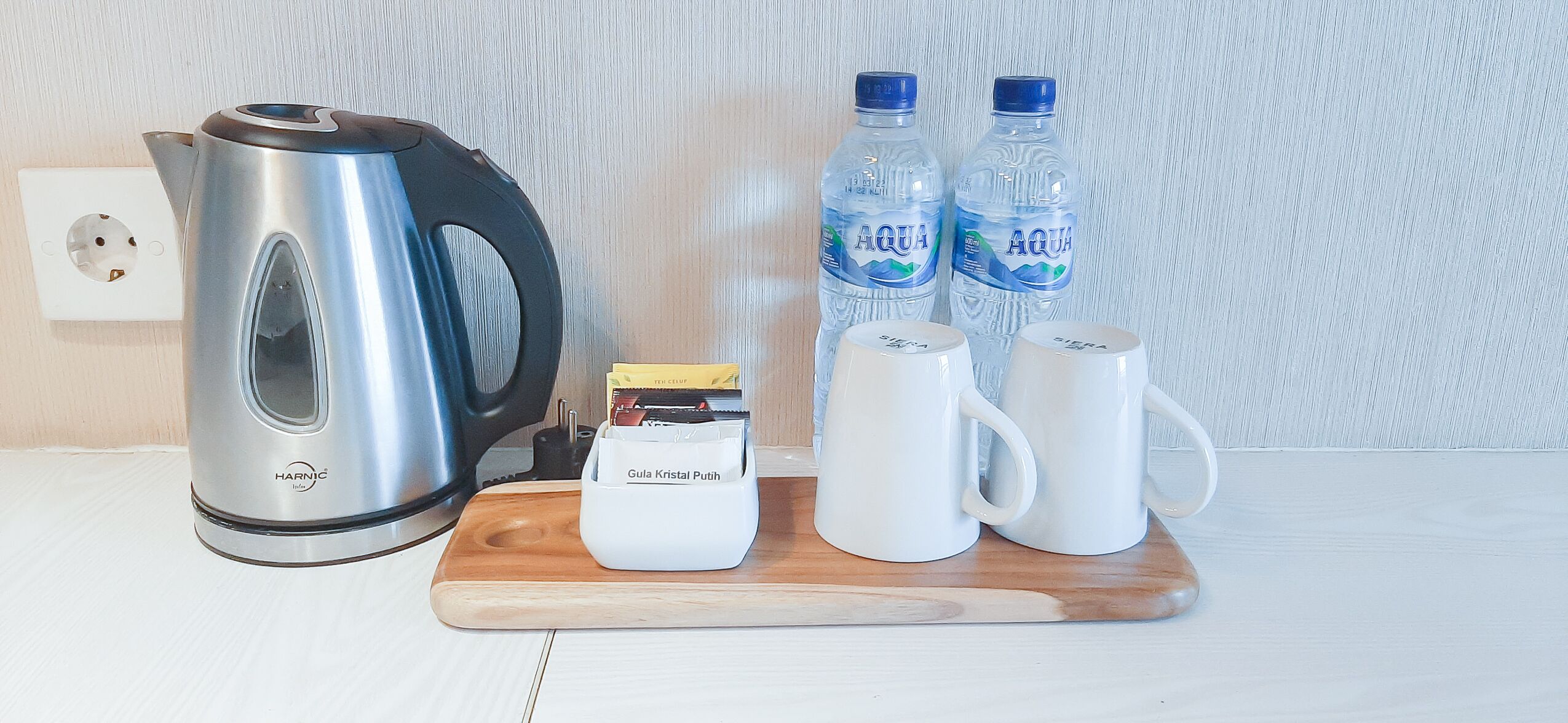 Un coin cuisine comprenant une bouilloire, deux bouteilles d’eau, une machine à café et deux tasses blanches posées sur une planche en bois.