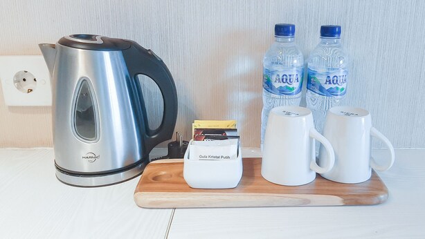 Una vajilla de cocina con un hervidor, dos botellas de agua, una cafetera y dos tazas blancas sobre una tabla de madera.
