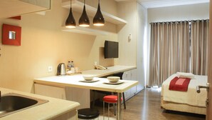 Une chambre d’hôtel moderne dotée d’une kitchenette, d’un coin repas et d’un lit recouvert d’une couverture rouge.