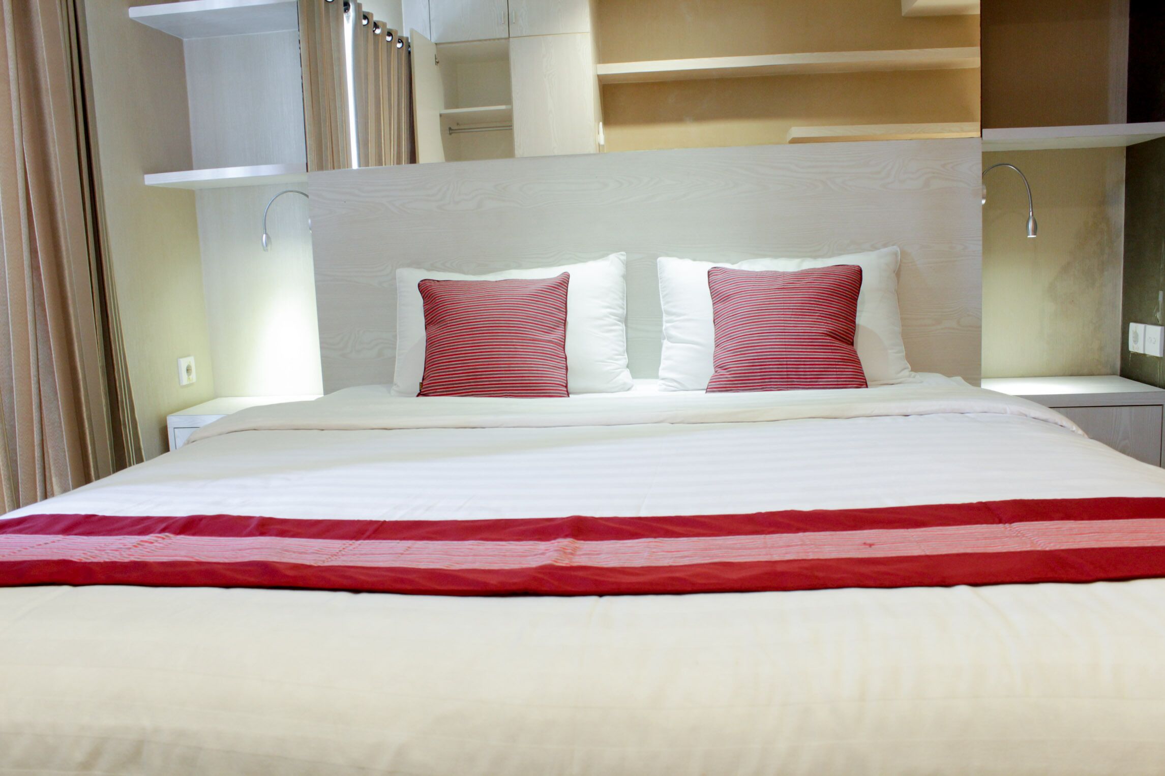 A hotel room with a large bed, two pillows, a red and white bedspread, and a white headboard.