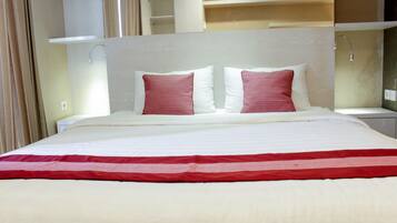 A hotel room with a large bed, two pillows, a red and white bedspread, and a white headboard.