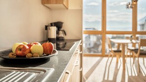 A kitchen with a fruit bowl on the counter, a coffee maker, and a view of the outdoors through large windows. - Friendly Apartment "Zirbe in the Nockerhof" with Mountain View, Wi-Fi & Terrace (Andrian)