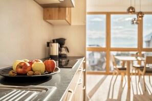 A kitchen with a fruit bowl on the counter, a coffee maker, and a view of the outdoors through large windows.