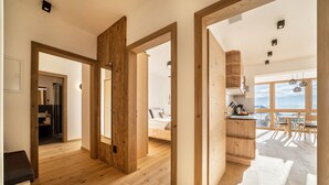 A spacious room with wooden flooring, a bed, a kitchen area with wooden cabinets, and a large window offering a view. - Friendly Apartment "Zirbe in the Nockerhof" with Mountain View, Wi-Fi & Terrace (Andrian)