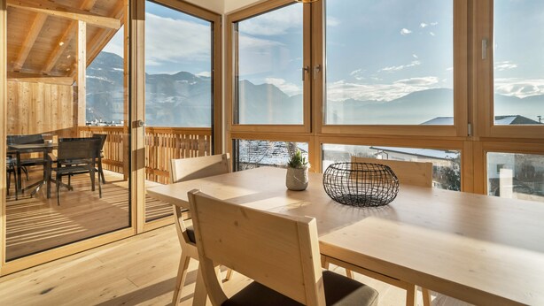 A wooden interior with large windows, a dining table, chairs, and a plant. - Friendly Apartment "Zirbe in the Nockerhof" with Mountain View, Wi-Fi & Terrace (Andrian)