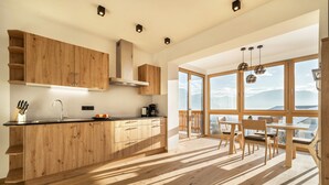 A modern kitchen with wooden cabinetry, a built-in stove, and a dining area with a view. - Friendly Apartment "Zirbe in the Nockerhof" with Mountain View, Wi-Fi & Terrace (Andrian)