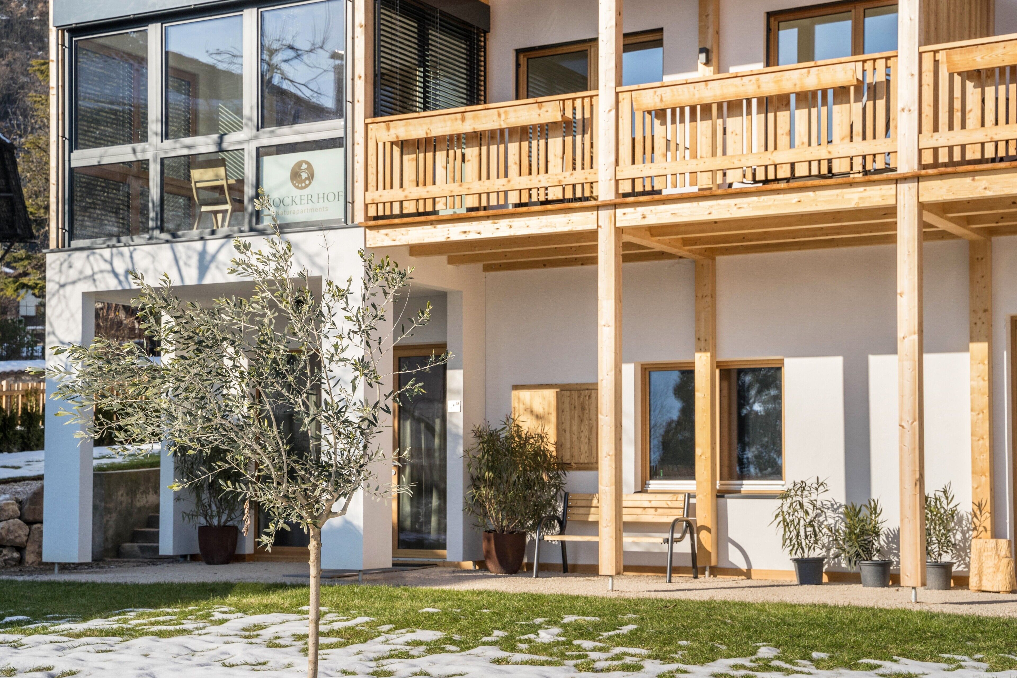 Un edificio moderno con un balcone in legno, ampie finestre e piante in vaso.