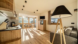 A modern kitchen with wooden cabinets, a dining area with a table and chairs, a sofa, and a large window with a view of mountains. - Welcoming Apartment "Eiche im Nockerhof" with Mountain View, Wi-Fi & Terrace (Andrian)