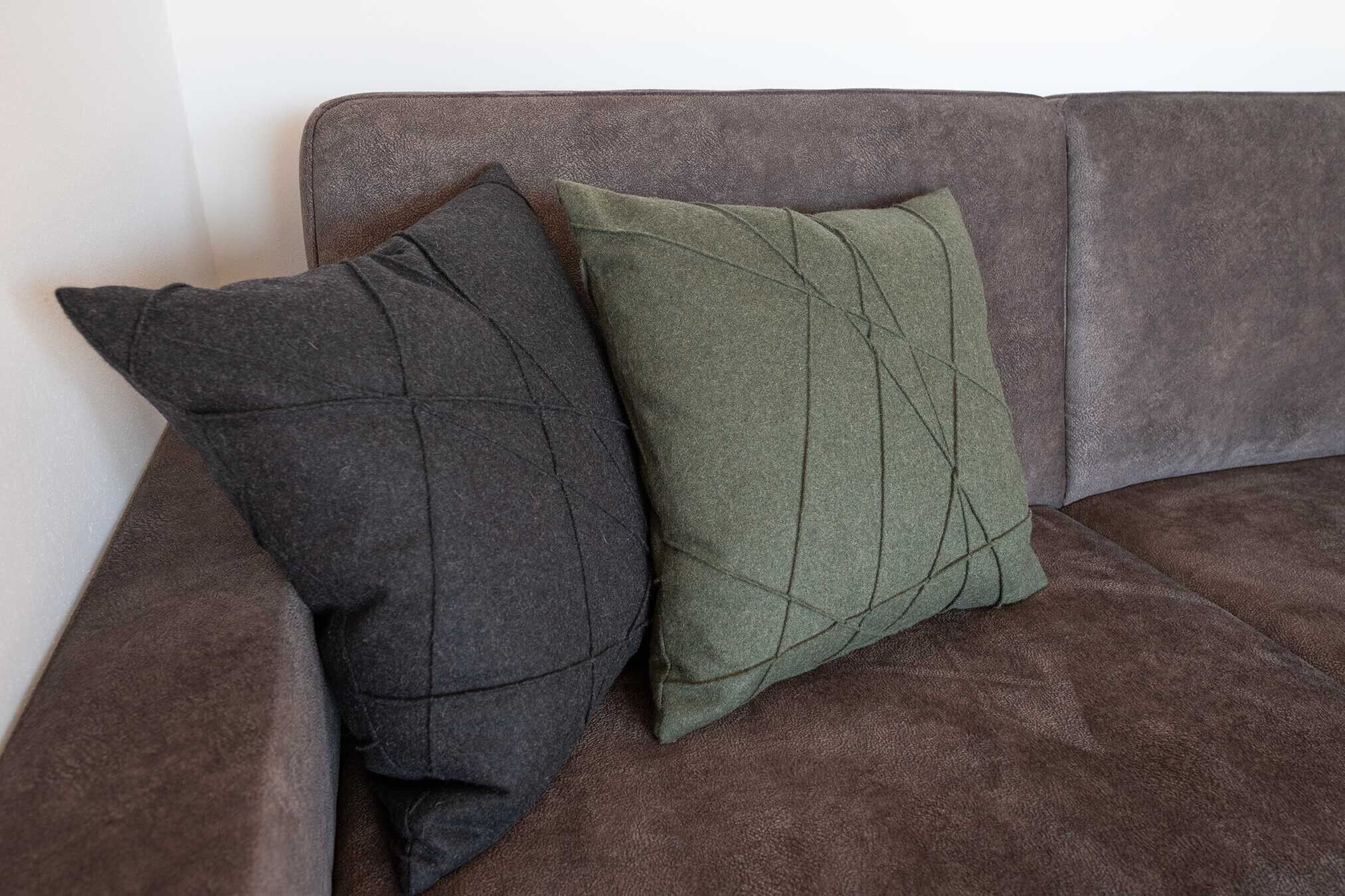 Ein braunes Sofa mit zwei Kissen, eines dunkel, eines grün.