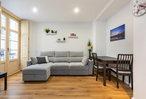 A living room with a grey sectional sofa, wooden dining table, chairs, and a clock on the wall.