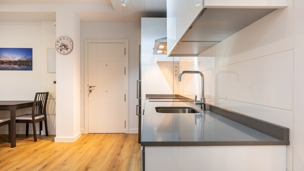 Une cuisine moderne dotée d’un évier encastré, d’un coin repas avec une table et des chaises en bois, et d’une porte blanche.