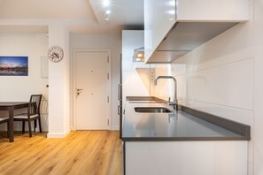 A modern kitchen with a built-in sink, a dining area with a wooden table and chairs, and a white door.