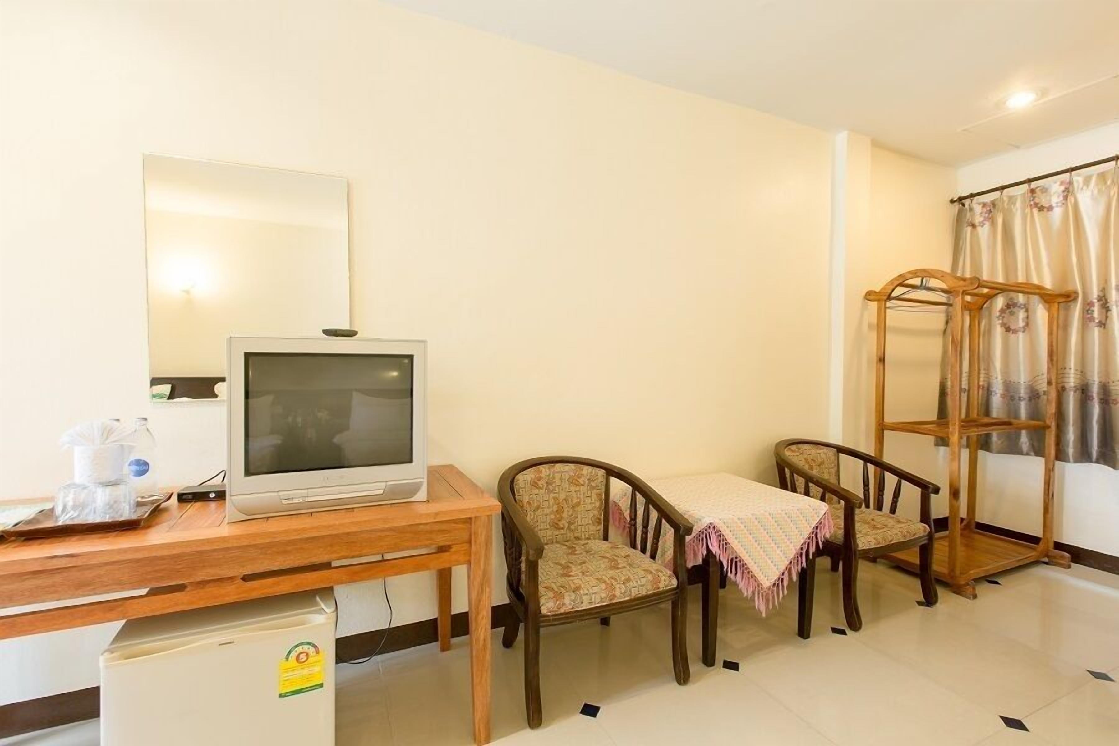 A room with a wooden desk, a television, two patterned chairs, a small refrigerator, and a wooden drying rack.