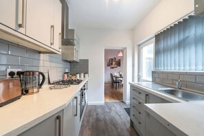 A modern kitchen with a central island, a dining area in the background, and a view through a window. - 3 BedRm Off Newland Ave Shop in Hull Sleeps 5 (Hull)
