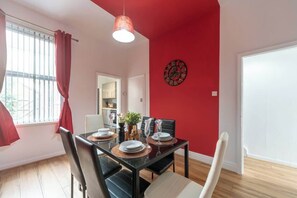 A dining area with a glass table, black and white chairs, a red wall with a clock, and a window with red curtains. - 3 BedRm Off Newland Ave Shop in Hull Sleeps 5 (Hull)