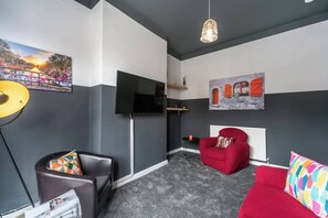 A modern living room with a flat-screen TV, a red sofa, a red armchair, and a colorful cushion. - 3 BedRm Off Newland Ave Shop in Hull Sleeps 5 (Hull)