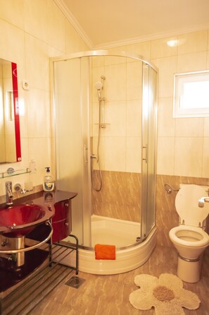 Une salle de bain avec une douche à parois de verre, un lavabo rouge et des toilettes blanches.