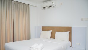 A hotel room with a bed, white linens, a headboard, a nightstand, and an air conditioning unit. - Homey and Modern Tamansari Semanggi 2BR Apartment (Jakarta)