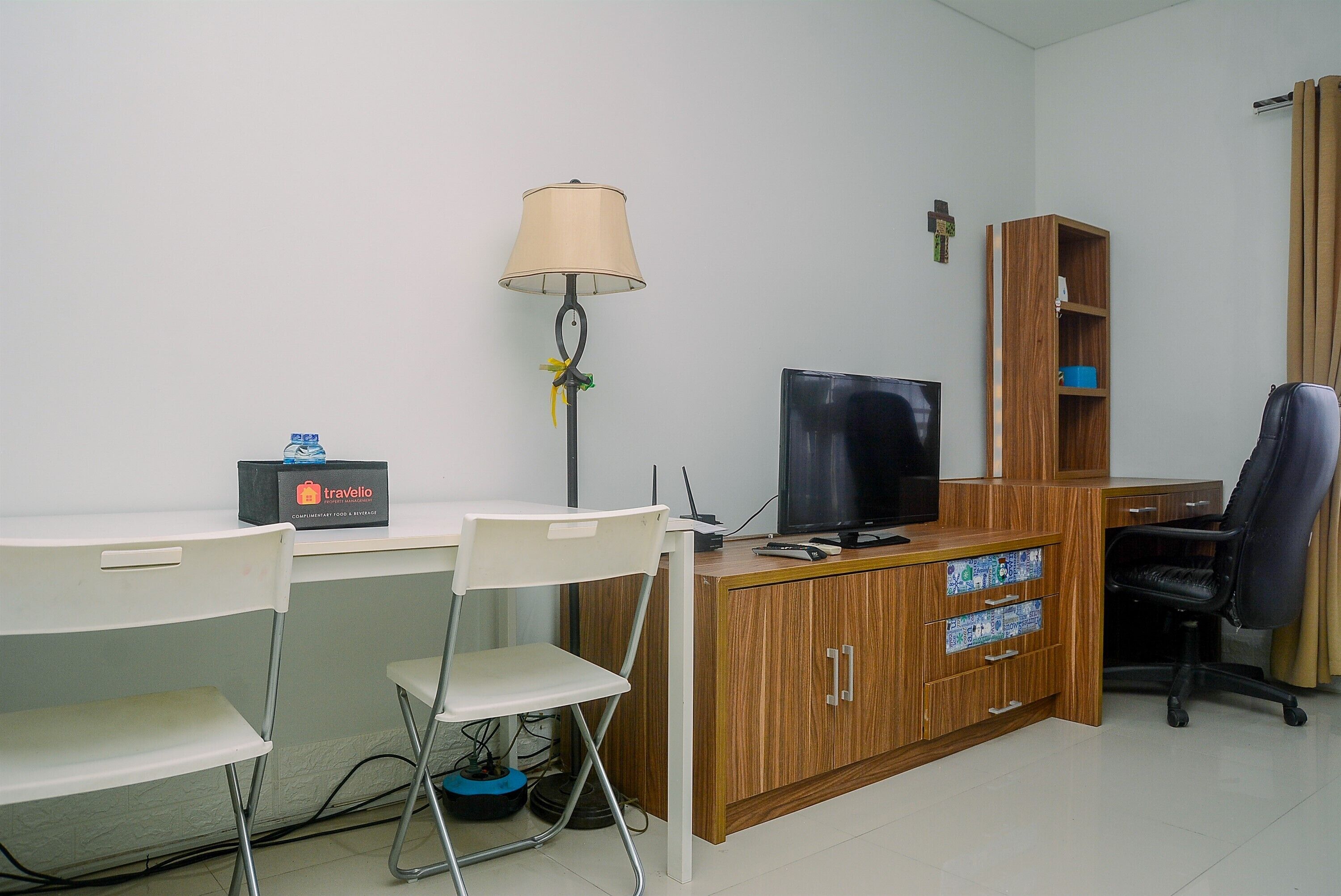 A small office with a desk, two chairs, a television, a lamp, and a bookshelf.