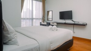 A hotel room with a bed, a desk with a chair, a TV, and a window with curtains.