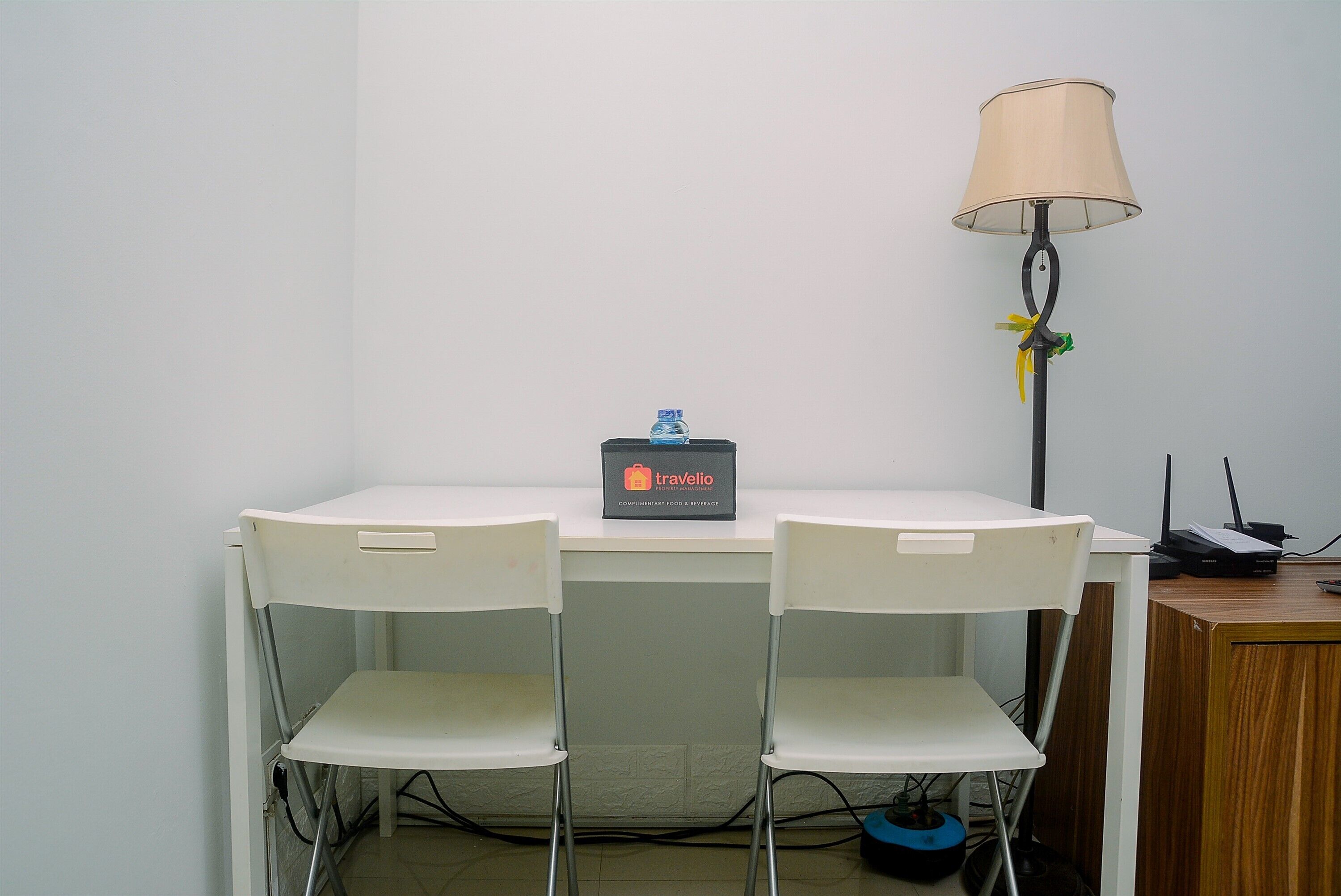A small table with two white chairs, a lamp, and a sign for 'Travelio'.