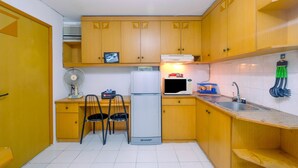 A compact kitchen with wooden cabinets, a refrigerator, a microwave, a sink, and a fan. - New Furnished 1BR Rajawali Apartment (Jakarta)